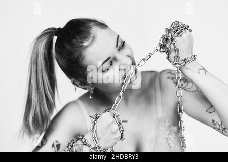 Tatouée femme féministe dans le soutien-gorge piquant et déchirant une chaîne de fer sur fond blanc.Concept de puissance de fille.Photo en noir et blanc Banque D'Images