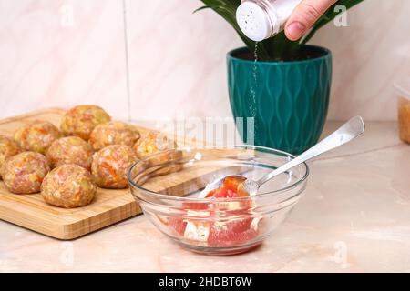 Un homme verse le sel d'un saupoudreur dans une sauce pour faire cuire des petits pains de chou paresseux dans une mijoteuse. Banque D'Images