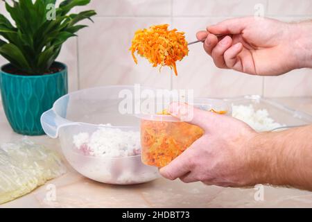 Un homme ajoute des oignons frits et des carottes à la viande hachée dans un bol pour les petits pains au chou paresseux sur la table. Banque D'Images