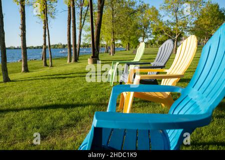 Chaises adirondack colorées sur l'herbe verte près de la rive d'un magnifique lac du Minnesota lors d'une soirée ensoleillée. Banque D'Images