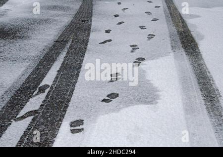 Pistes noires des pneus de voiture et empreintes de pas dans la neige sur la route asphaltée Banque D'Images