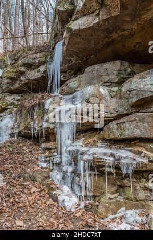 Glace congelée qui descend dans la formation de mur de roche le long de la piste dans les montagnes dégeler et geler sur le sol par une journée froide en hiver Banque D'Images