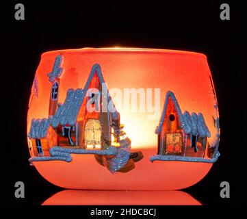 Une tasse en verre peinte à la main avec un décor hivernal éclairé par une bougie à l'intérieur de la tasse.Un gros plan photographique utilisant la peinture légère. Banque D'Images