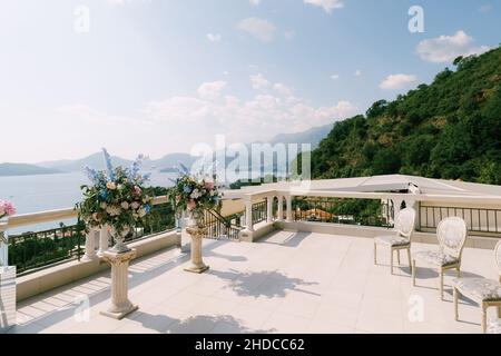 Bouquets de fleurs devant des chaises anciennes sur une terrasse donnant sur la mer et les montagnes Banque D'Images