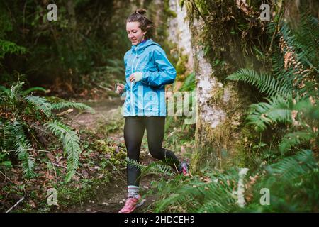 La coureuse de sentier en blouson bleu court dans une forêt luxuriante de fougère Banque D'Images