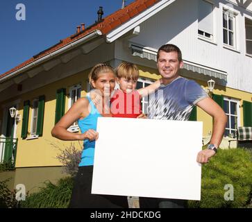 Junge Familie mit vor type neugekauftem Haus, hält weisses Schild, frei für beliebigen Texte, 30,35, 5 Jahre, M.:Oui Banque D'Images