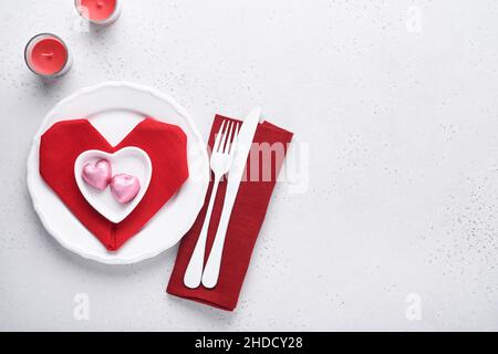 Table de jour de Valentinas couleur blanche avec argenterie blanche, serviette rouge pliée comme coeur, bougies, champagne, verres sur fond blanc pour greeti Banque D'Images