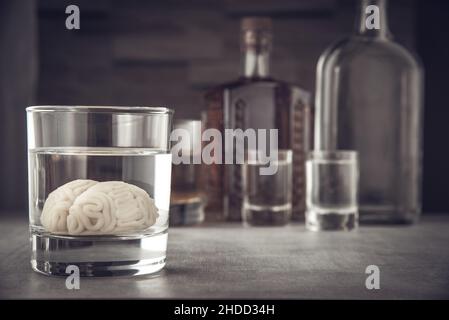 Modèle de cerveau humain dans un verre avec une boisson alcoolisée, sur fond de bouteilles avec de l'alcool.Dépendance à l'alcool.Dommages causés par l'alcool au cerveau. Banque D'Images