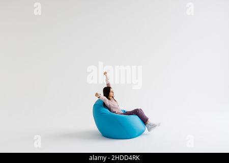 Jeune fille couchée avec les mains levées sur le sac de beanbag isolé sur fond blanc. Banque D'Images