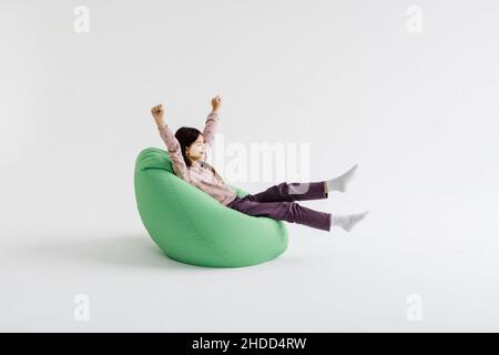 Jeune fille couchée avec les mains levées sur le sac de beanbag isolé sur fond blanc. Banque D'Images