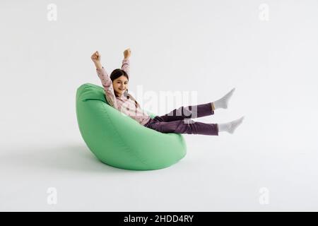 Jeune fille couchée avec les mains levées sur le sac de beanbag isolé sur fond blanc. Banque D'Images