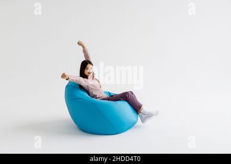 Jeune fille couchée avec les mains levées sur le sac de beanbag isolé sur fond blanc. Banque D'Images