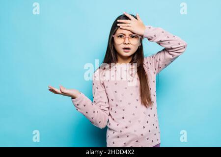 Horrible, stress, choc.Portrait émotionnel fou beau caucasien petite fille portant une robe rayée sur fond bleu clasping tête dans les mains.E Banque D'Images