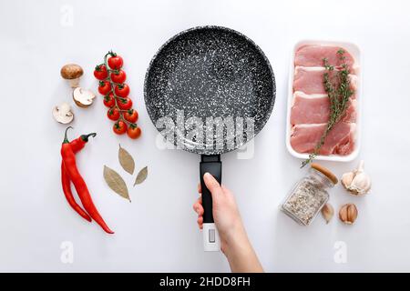 Femme tenant main poêle en marbre noir et produits sur fond gris, vue du dessus Banque D'Images