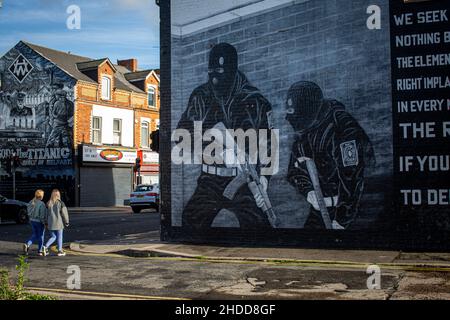 Deux jeunes femmes marchant devant une fresque paramilitaire loyaliste sur la route Newtownards le 8th novembre 2021 à Belfast, Irlande du Nord . Banque D'Images