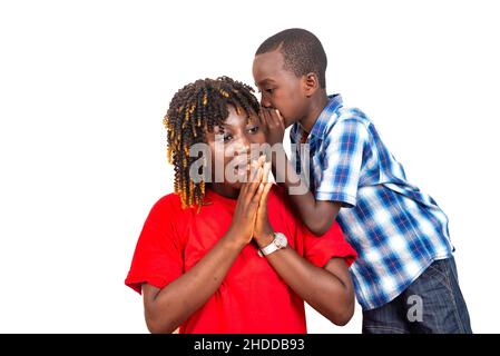 un petit garçon mignon racontant un secret de famille à l'oreille de sa mère surprise avec ses mains jointes à l'intérieur. Banque D'Images