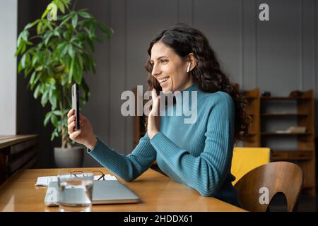 Une employée positive qui profite d'une conversation vidéo sur son smartphone avec un ami de sa famille pendant sa pause professionnelle Banque D'Images