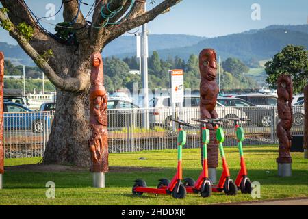 Tauranga Nouvelle-Zélande - janvier 2 2022; quatre trottinettes de location alignées sur le Strand devant des totems maoris sculptés traditionnels connus sous le nom de Matariki sh Banque D'Images