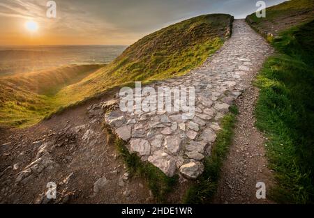 Le soleil d'été se levant au-dessus de la campagne du Worcestershire, lumière du soleil brillant à faible angle sur un chemin rocheux escarpé menant à Worcestershire Beacon, par Banque D'Images