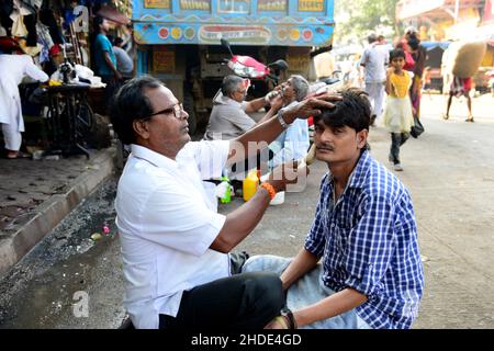 Un barbier de rue rasant son client à Mumbai, Inde. Banque D'Images