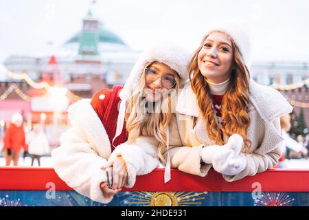 Jeunes femmes heureuses filles génération z avec des cheveux bouclés en blanc vêtements chauds avoir du plaisir en hiver patinoire décorée de lumières Banque D'Images