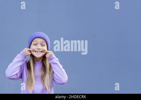 Un enfant qui montre une dent de lait manquée.Changer de concept de dents.Jolie petite fille caucasienne aux cheveux blonds de huit ans sur fond violet avec espace de copie Banque D'Images