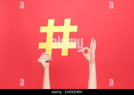 Les femmes tiennent le grand hashtag jaune et le doigt pointant vers lui montrant le signe correct, isolé sur le mur rouge de fond de studio.Markétine sur les médias sociaux Banque D'Images