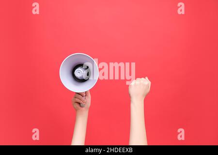 Gros plan des mains féminines tenant le mégaphone et élevé poing, protestation politique de montrer son pouvoir, isolé sur fond rouge studio avec espace de copie Banque D'Images