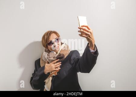 Belle baby-boomer femme d'âge moyen dans des lunettes de soleil prend selfie sur smartphone en plein soleil. Banque D'Images