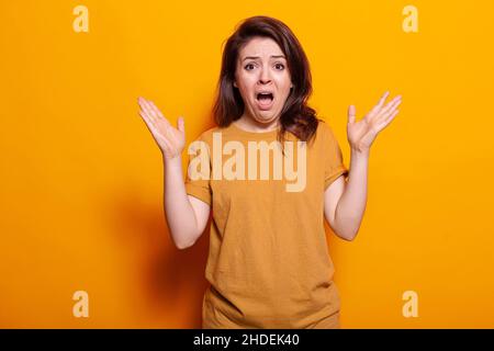 Personne effrayée montrant une expression faciale choquée, debout sur fond orange.Femme inquiète se sentant effrayée et terrifiée tout en regardant l'appareil photo.Adulte paniqué avec les mains vers le haut Banque D'Images