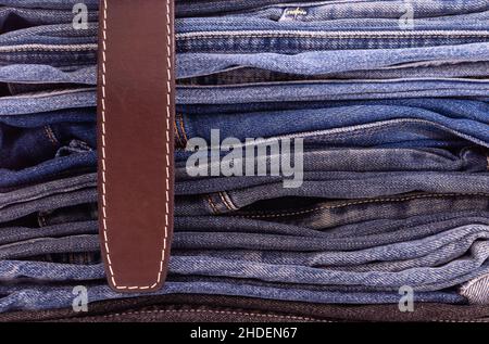 Ceinture en cuir gros plan sur une pile de pantalons en denim de différents modèles et couleurs.Vue latérale Banque D'Images