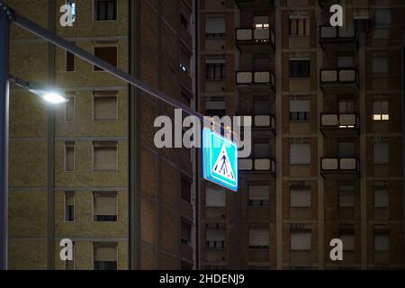 Panneau de signalisation à la lumière vive devant un immeuble résidentiel avec fenêtres éclairées la nuit. Banque D'Images