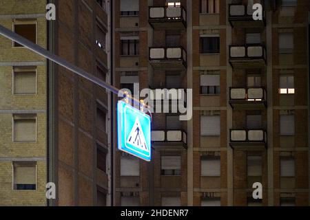 Panneau de signalisation à la lumière vive devant un immeuble résidentiel avec fenêtres éclairées la nuit. Banque D'Images