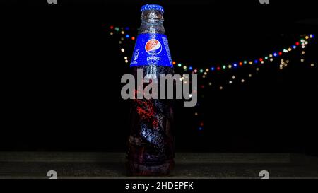 Gros plan d'une bouteille en verre Pepsi isolée sur un fond noir avec des lumières colorées Banque D'Images