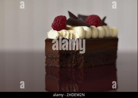 Délicieux gâteau avec deux framboises et morceaux de chocolat croustillants sur une table rouge foncé Banque D'Images