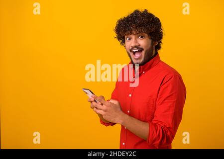 Drôle surpris gars branché soudainement lire le message sur son téléphone mobile et exprimant l'étonnement de choc, des nouvelles incroyables sur smartphone.Studio tourné isolé Banque D'Images