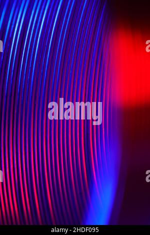 Gros plan des anneaux de ressort en métal enroulé à l'état comprimé en lumière rouge et néon, photo macro Banque D'Images