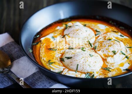 Œufs pochés turcs, Cilbir, sur du yaourt grec, assaisonnés de paprika et de beurre fondu et garnis de feuilles de menthe.Arrière-plan flou. Banque D'Images