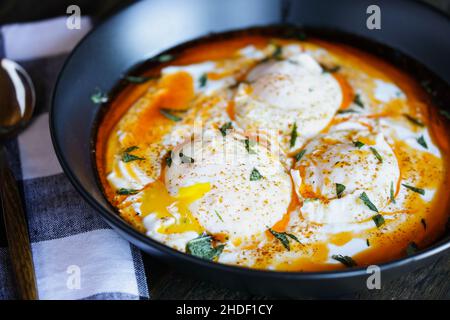 Œufs pochés turcs, Cilbir, sur du yaourt grec, assaisonnés de paprika et de beurre fondu et garnis de feuilles de menthe.Arrière-plan flou. Banque D'Images