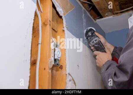 Entretien réparation travaux de remplacement cloison sèche endommagée sur la découpe des ouvriers plaques de plâtre avec outils électriques de construction Banque D'Images