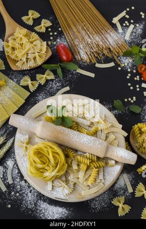 Divers de pâtes ou macaroni sur une surface noire avec menthe fraîche, tomates cerises et mini-pâte et broche roulante sur l'image verticale Banque D'Images