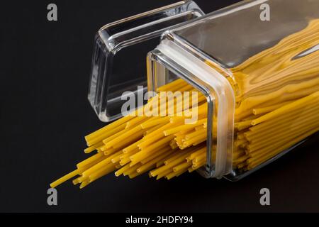 Non cuits, sécher diverses tailles de pâtes spaghetti dans un grand pot en verre sur une surface noire avec un espace de copie Banque D'Images