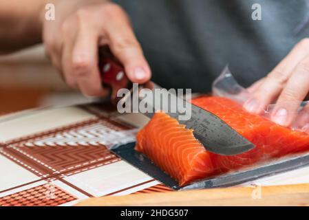 La main avec un couteau coupe le saumon rouge pour les sushis Banque D'Images