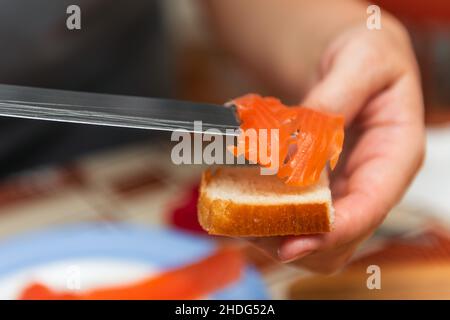 La main avec un couteau coupe le saumon rouge pour les sushis Banque D'Images