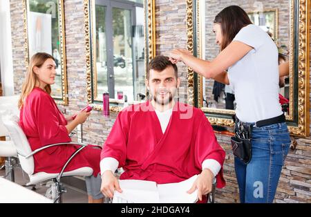 Portrait de l'homme coiffeur professionnel près de la femme client avec magazine en salon Banque D'Images