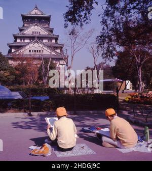 1960s, historique, deux garçons japonais sur une sortie scolaire ou sur le terrain assis sur le sol dessinant une photo d'un temple, le Japon. Banque D'Images