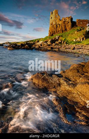 La lumière de la fin de soirée projette une lumière chaude sur les murs du château de Dunure tandis que la mer se balade doucement sur les rochers.Un bel endroit lors d'une soirée glorieuse. Banque D'Images