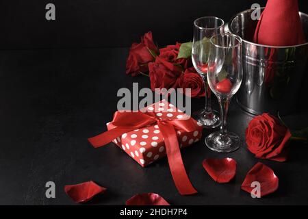 Saint-Valentin avec champagne, cadeau, bouquet de roses rouges sur fond noir.Invitation de carte de vœux.Copier l'espace. Banque D'Images