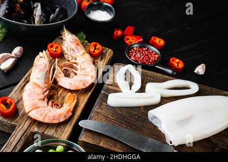 Ingrédients de paella espagnole non cuits avec crevettes royales, seiches, moules et herbes sur une table en bois noir, photo de nourriture. Banque D'Images