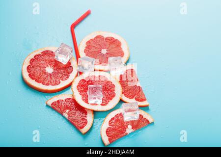 Tranches de pamplemousse et cubes de glace avec une paille sur fond bleu en forme de cocktail.Le concept de la boisson à la limonade est un rafraîchissement d'été Banque D'Images